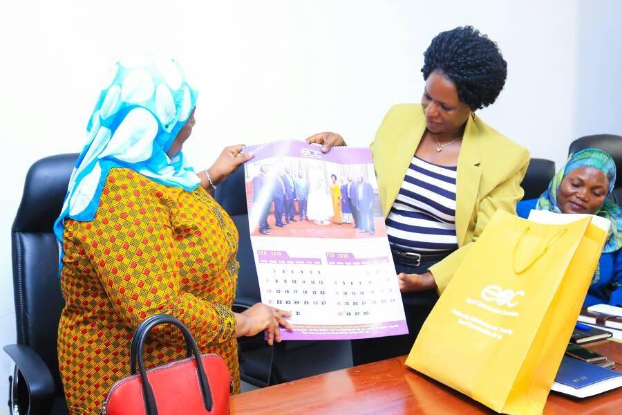 The Chairperson, Mrs. Sylvia Muwebwa Ntambi handing over the EOC calendar to the Minister.